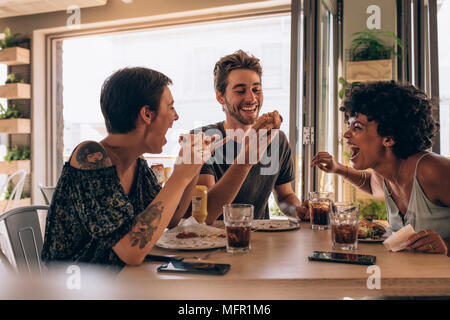 Groupe d'amis ayant burger du restaurant. Cheerful young people eating hamburger et bénéficiant à un fast-food. Banque D'Images