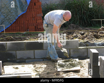 Builder / travailleur de la construction travaillant sur un mur de briques briques thermalite cimentation dans modèle libération Banque D'Images