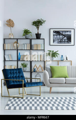 Salon lumineux avec un intérieur bleu marine, fauteuil design avec cadre en métal, d'or, vases de verre et de plantes en pot sur une bibliothèque Banque D'Images