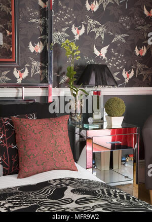 Sur la lampe de chevet miroir métal table à côté d'un lit double dans la chambre rouge et noir avec du papier peint de style chinois Banque D'Images