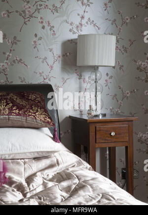 Sur la lampe de chevet en bois table à côté de lit avec tête de lit en cuir dans un style traditionnel avec papier peint Motif floral Banque D'Images