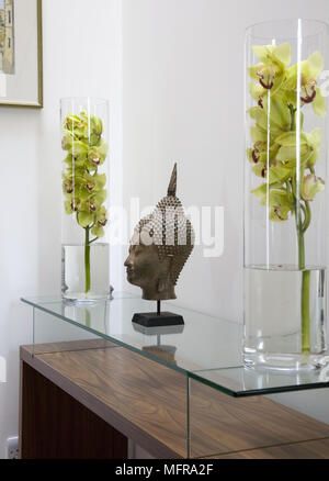 Paire de vases en verre dans les arrangements de fleurs de chaque côté de la tête de Bouddha figure sur verre surmontée side table Banque D'Images