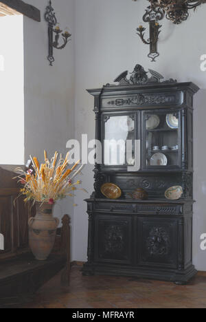 Armoire avec portes en verre ornés d'afficher à côté de la vaisselle vase de fleur sur banc en bois Banque D'Images