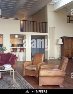 Spacieuse, coin salon décloisonné avec plancher de bois, fauteuils en cuir, d'un bar avec tabourets, loft, niveau supérieur et un plafond à poutres apparentes. Banque D'Images