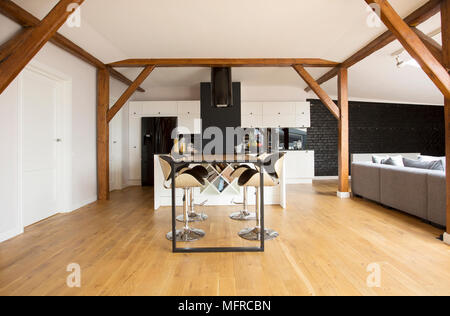 Tabourets de bar moderne et tableau noir situé dans le grenier de l'intérieur appartement avec parquet, poutres apparentes et canapé gris Banque D'Images