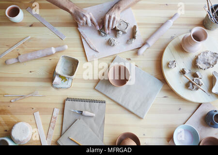 Directement au-dessus de la céramiste méconnaissable malpropre assis à table en bois et d'argile de coupe avant de faire de l'artisanat Banque D'Images
