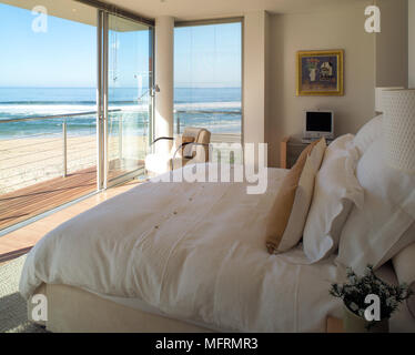 Un point mort moderne chambre à coucher avec lit double portes coulissantes en verre donnant sur balcon en bois donnant sur l'océan Banque D'Images