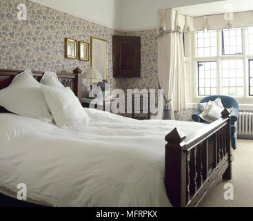 Pays traditionnels, chambre avec un papier peint fleuri, baie vitrée, rideaux et un lit en bois avec literie brodée. Banque D'Images