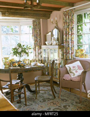 Salle à manger avec table et chaises sur tapis à motifs floraux rideaux de chintz et poutres apparentes au plafond. Banque D'Images