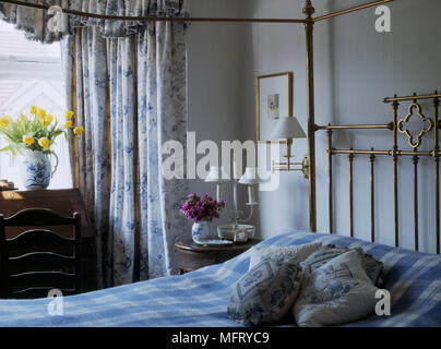 Chambre bleue avec un lit double à baldaquin en laiton vérifier floral couvre-lit rideaux ouverts table côté coussins lampes Banque D'Images