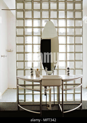 Miroir ovale au-dessus d'un lavabo dans l'unité d'acier contre brique de verre mur séparant espace douche Banque D'Images