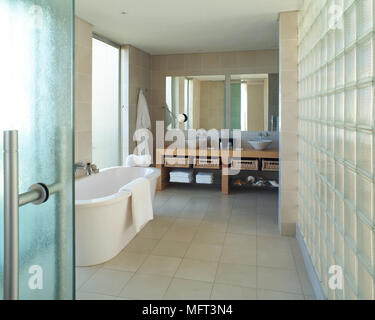 Une salle de bains moderne avec baignoire sur pied deux lavabos situé sur l'unité bois carrelage mur de blocs de verre Banque D'Images