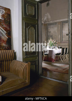 Voir à travers les portes à panneaux d'un coin salon pour une salle à manger traditionnelle avec des murales peintes et une table à manger et chaises. Banque D'Images