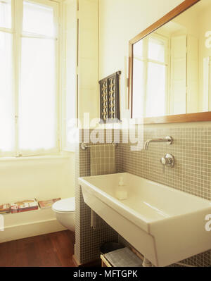 Lavabo fixé sur mur carrelé avec miroir au-dessus de toilettes et partition derrière Banque D'Images