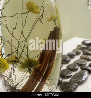 Vase en verre contenant des fleurs et des bâtons sur table avec galets polis Banque D'Images