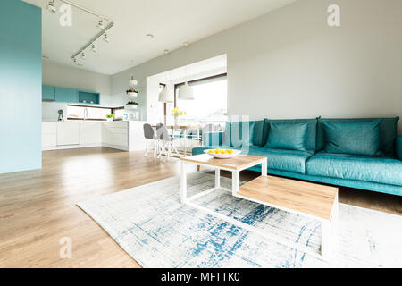 Blanc et turquoise espace ouvert de l'intérieur de la chambre avec grand canapé, cuisine moderne et d''une table à manger par de grandes fenêtres Banque D'Images