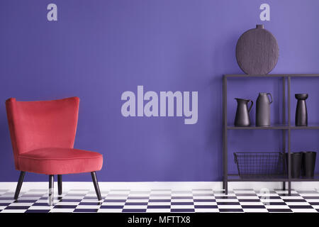Véritable photo d'un salon coloré avec de l'intérieur, fauteuil en velours rouge et noir avec décorations rack contre un mur ultra violet Banque D'Images