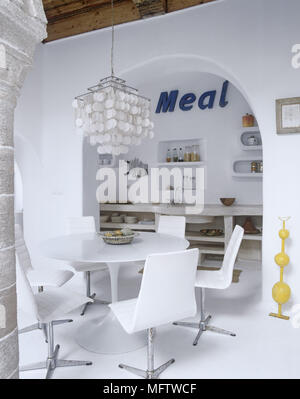 Un cadre rustique salle à manger aux murs blanchis à la chaux contrastent avec des arcades en pierre rétro moderne table et chaises en plastique blanc dans la région de cuisine Banque D'Images