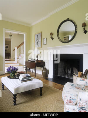 Un salon avec un miroir ovale au-dessus d'une cheminée ouverte avec une grande couverture et un petit siège rembourré. Banque D'Images