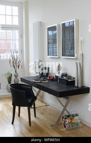 Accueil espace bureau avec deux images encadrées au-dessus d'un bureau et chaise noir sur un sol en bois. Banque D'Images