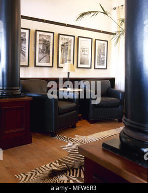 Salon traditionnel avec des colonnes, des fauteuils en cuir, tableaux, et une couverture de peau animale. Banque D'Images