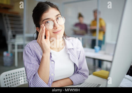 Portrait de jeune travailleur occasionnel dans les lunettes sitting at office Banque D'Images