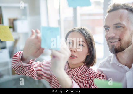 Business couple debout devant un mur de verre avec post it et discuter Banque D'Images