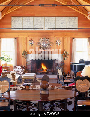 Chaises et table et piano en face de cheminée avec feu allumé dans le salon de style rustique Banque D'Images