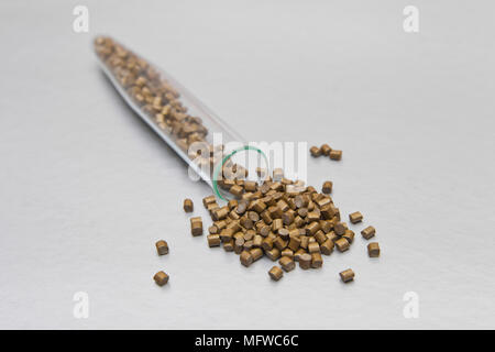 Palettes en plastique . Colorant pour polymères en granules. La mère de la perle d'or de granules de plastique brut déversé de l'industrie en dehors du tube Banque D'Images