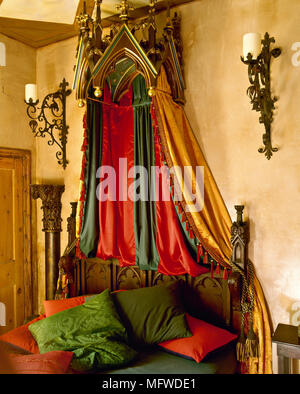 Une chambre à coucher de style gothique avec des murs jaunes, des poutres au plafond, couvert d'or, rouge, vert, fer à repasser le linge de lit, des appliques bougie Banque D'Images