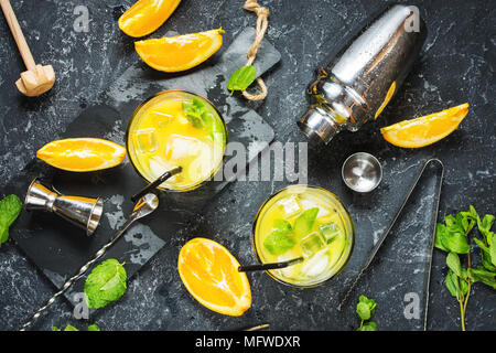 Boissons froides cocktail d'été avec orange et menthe dans les verres et sur la pierre sombre arrière-plan. Bar à cocktails, des outils shaker, verres, menthe l Banque D'Images