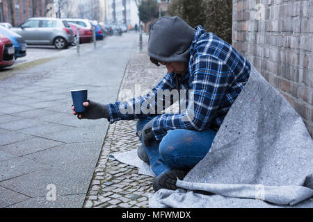 La main de mendiant portant des gants Holding Disposable Cup Banque D'Images