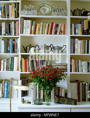 Détail de livres, de bibelots knick, et un bouquet de fleurs peint en blanc sur des étagères. Banque D'Images