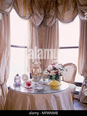 Table ronde avec plateau en verre en baie vitrée avec rideaux swag habillé Banque D'Images