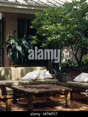 Sofas face table basse en bois sur le carrelage de la cour avec des arbres et arbustes en pots Banque D'Images