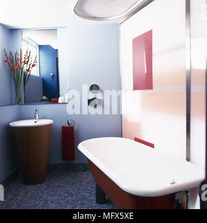 Salle de bains carrelée moderne, avec un haut rouleau baignoire, bleu, et un lavabo dans un cabinet cylindrique. Banque D'Images