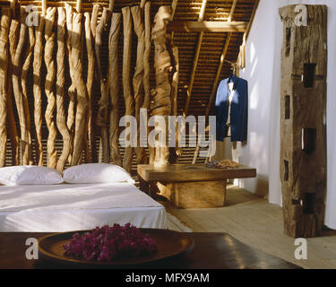 Table en bois lourd à côté d'un lit double sur le sol avec des pièces sculpturales rustique Banque D'Images