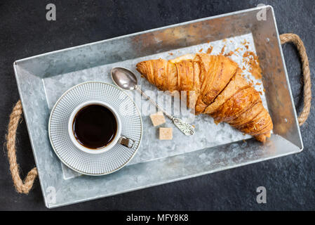Petit-déjeuner léger de croissants frais et une tasse de café sur le plateau gris Banque D'Images