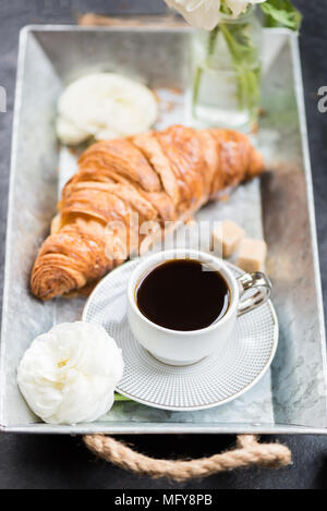 Petit-déjeuner léger de croissants frais et une tasse de café sur le bac gris, Ranunculus fleurs à proximité Banque D'Images