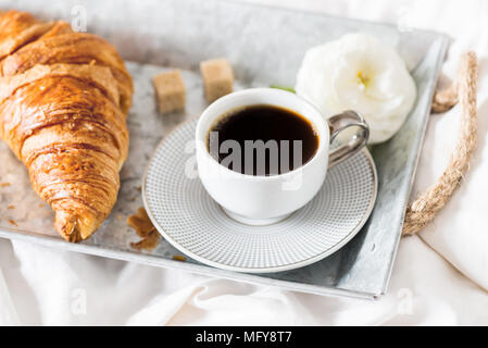 Petit-déjeuner au lit de croissants frais et une tasse de café sur le bac gris, Ranunculus fleurs à proximité Banque D'Images