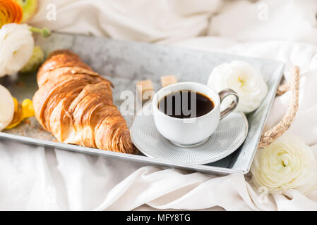 Petit-déjeuner au lit de croissants frais et une tasse de café sur le bac gris, Ranunculus fleurs à proximité Banque D'Images