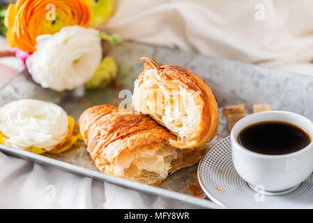Petit-déjeuner au lit de croissants frais et une tasse de café sur le bac gris, Ranunculus fleurs à proximité Banque D'Images