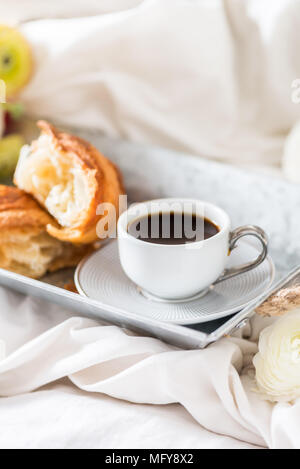 Petit-déjeuner au lit de croissants frais et une tasse de café sur le bac gris, Ranunculus fleurs à proximité Banque D'Images