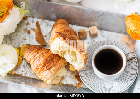 Petit-déjeuner au lit de croissants frais et une tasse de café sur le bac gris, Ranunculus fleurs à proximité Banque D'Images