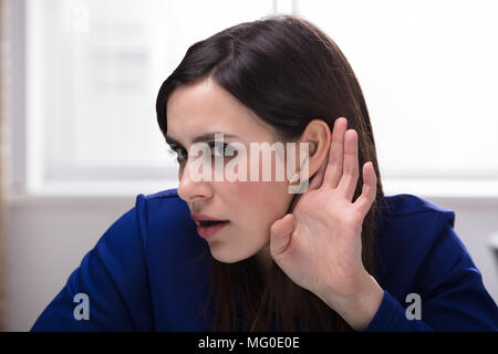 Close-up of a young woman essaie d'écouter avec l'oreille de la main Banque D'Images