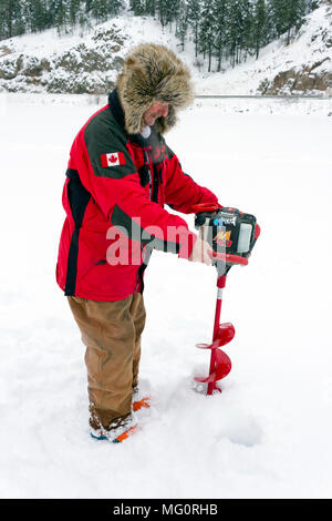 Yellow Lake, Colombie-Britannique, Canada - le 7 janvier 2018 : l'homme de percer un trou à travers la glace épaisse avec la vis et percer la glace pour la pêche à la truite sur un col Banque D'Images