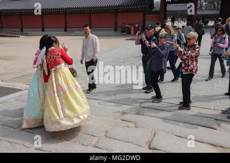 Un groupe de touristes rush plus de photographier deux jeunes femmes habillées de couleurs vives hanboks traditionnel coréen qui constituent à Séoul, Corée. Banque D'Images
