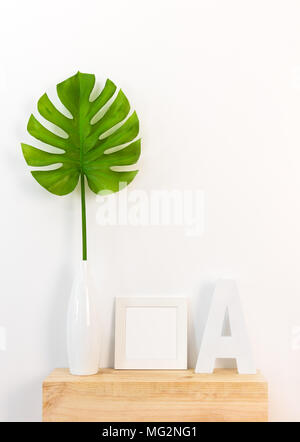 Décor à la maison avec un élégant cadre photo blanc, vert feuille tropicale dans un vase, et une lettre sur la surface en bois. Banque D'Images