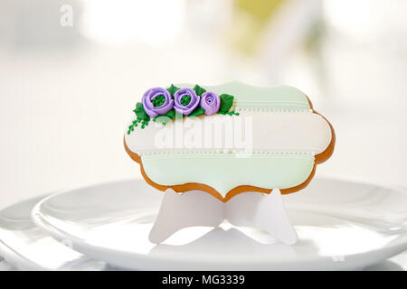 Cute gingerbread cookie sucré avec glaçure bleu et vert de fleurs et perles se dresse sur une assiette blanche sur une table de restaurant,couvert de snowwhite nappe. Décoration pour table de fête parfaite. Banque D'Images