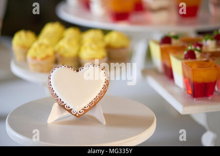 Close-up of a sweet gingerbread cookie,recouvert de glaçure blanche se trouve sur le support en bois en face de candybar festive avec cupcakes fruits rouges et jaunes gelées,décoré avec des framboises fraîches. Banque D'Images